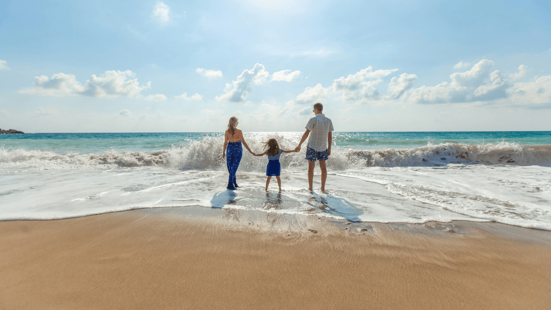 A family of three standing at the edge of the water on a beach