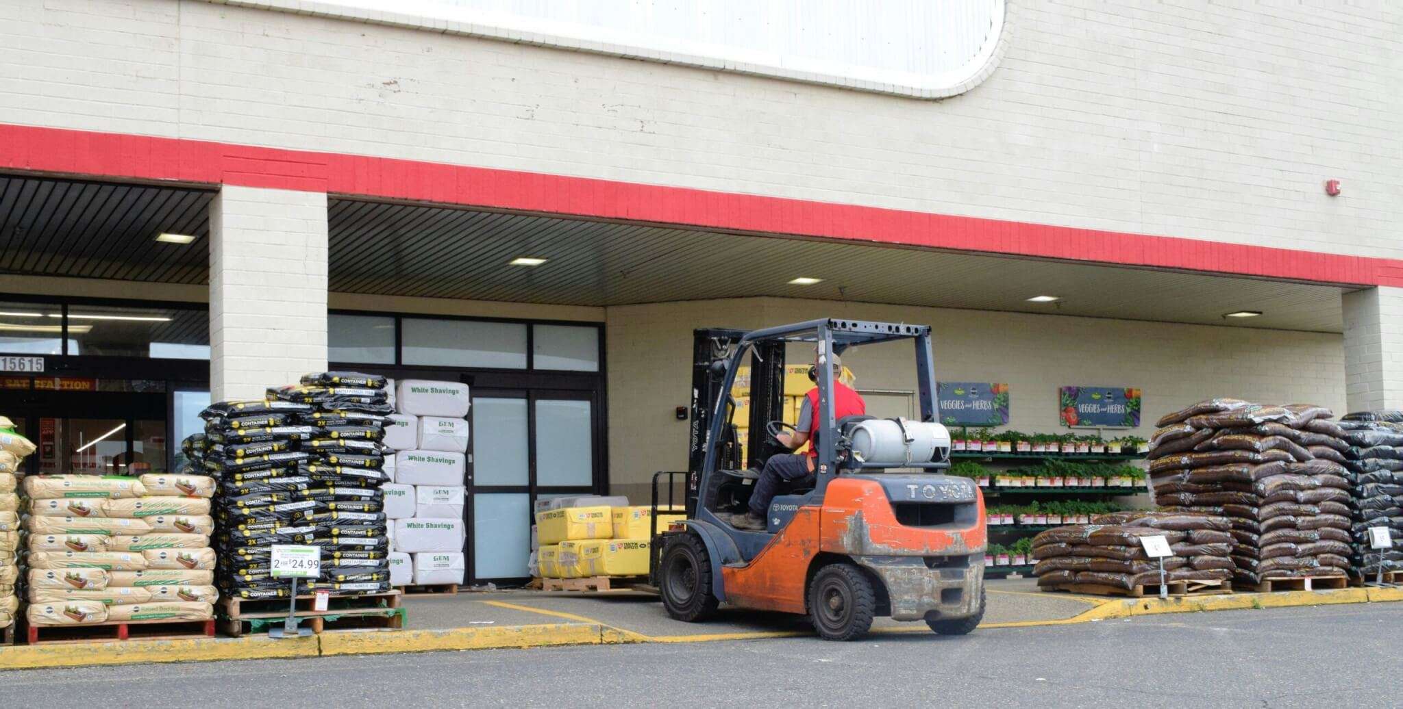 A worker driving a forklift outside a hardware store
