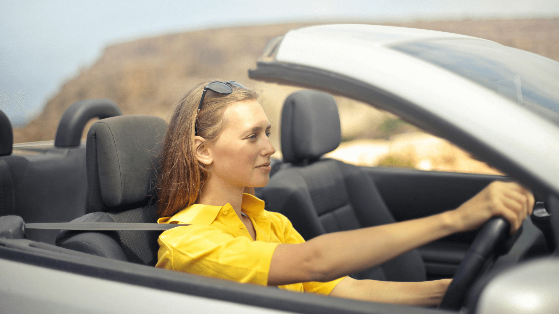 young women in a yellow shirt driving a convertible with the top down.