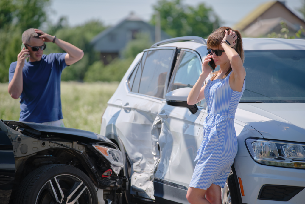 Two drivers on their phones after a car accident involving significant vehicle damage.