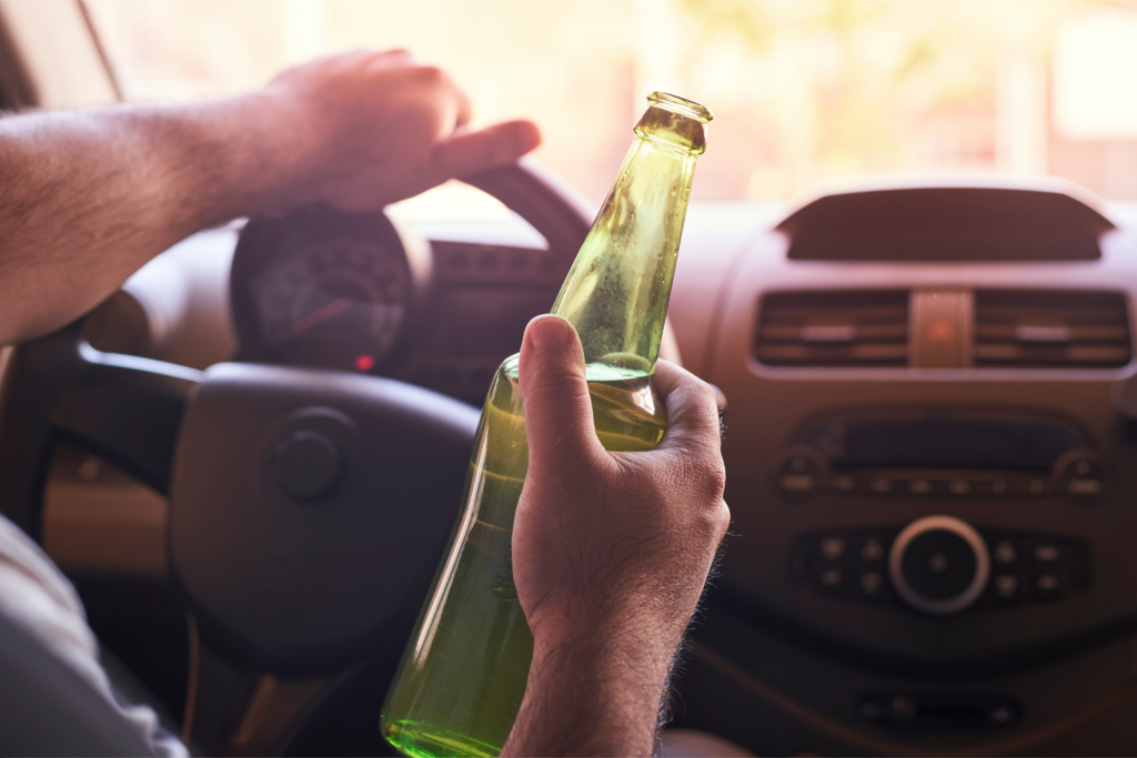 Driver holding a beer bottle while driving, representing the dangers of drunk driving