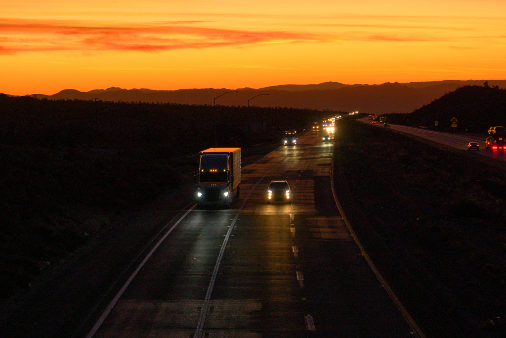 A semi-truck driving down a highway as it get closer to night