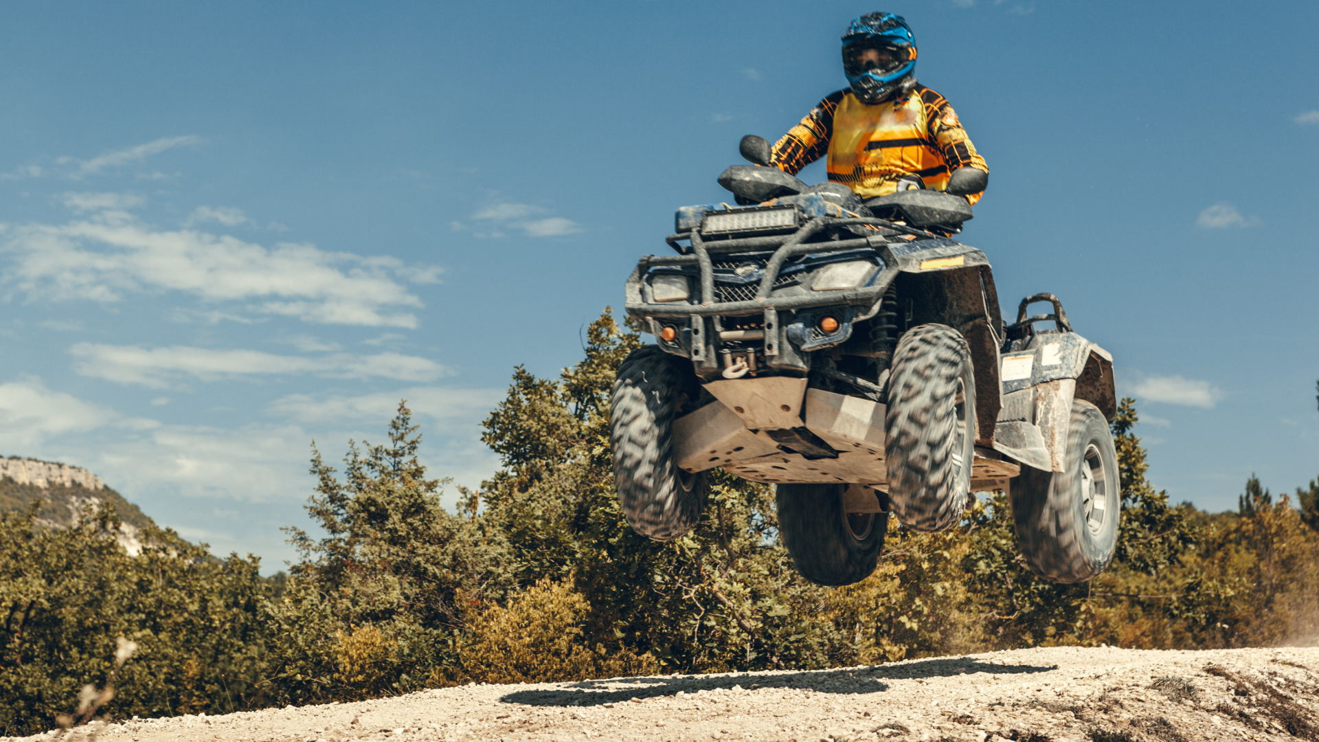 Rider in full gear jumping an ATV off a dirt trail in Montana backcountry on a sunny day