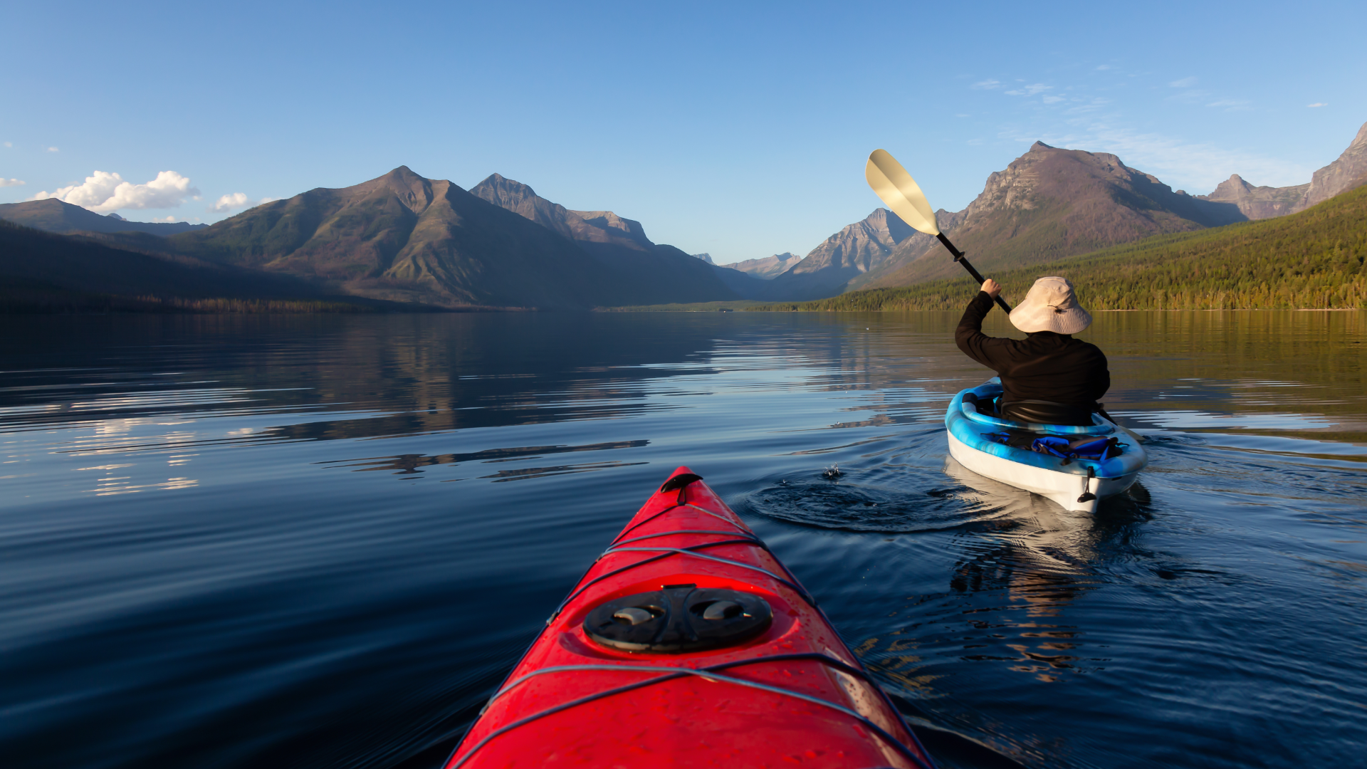 Two kayakers paddling on a calm Montana lake surrounded by mountains during summer