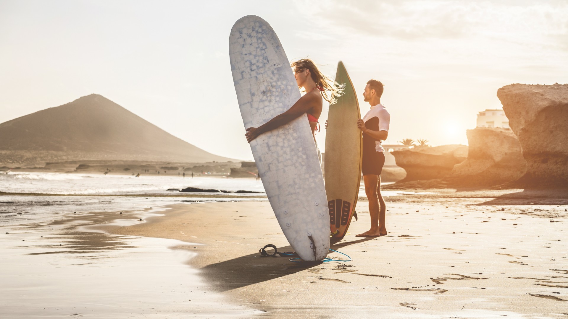 Two people standing on a beach holding surfboards near the shoreline.