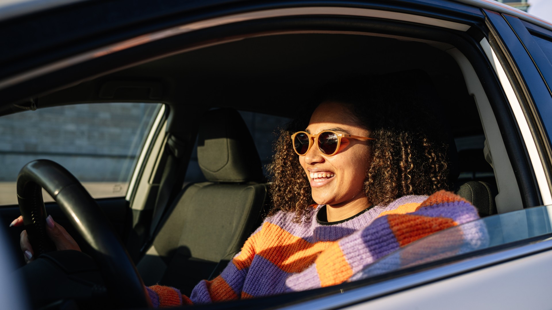 Person wearing sunglasses smiling while driving a car.