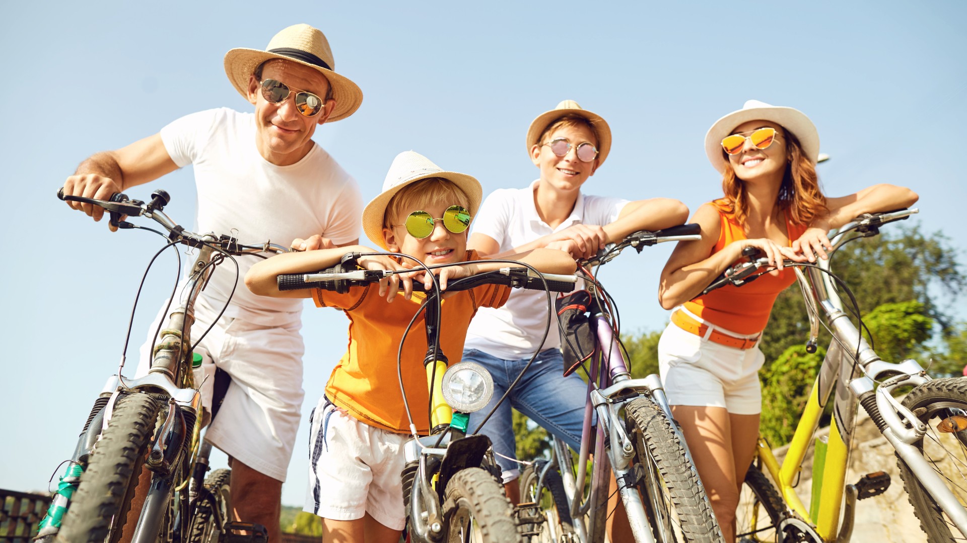 Family standing outdoors with bicycles on a sunny day.