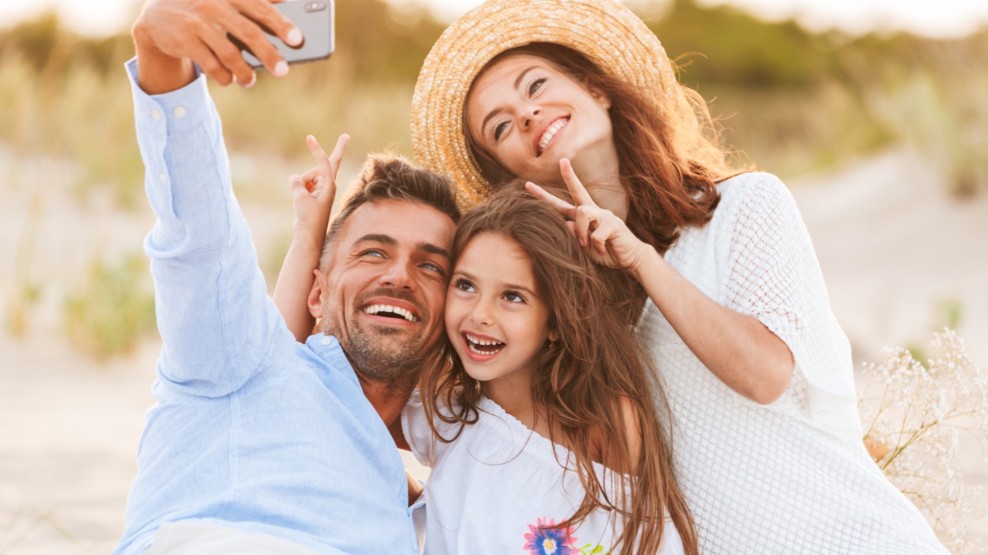 Family smiling and taking a selfie together outdoors.