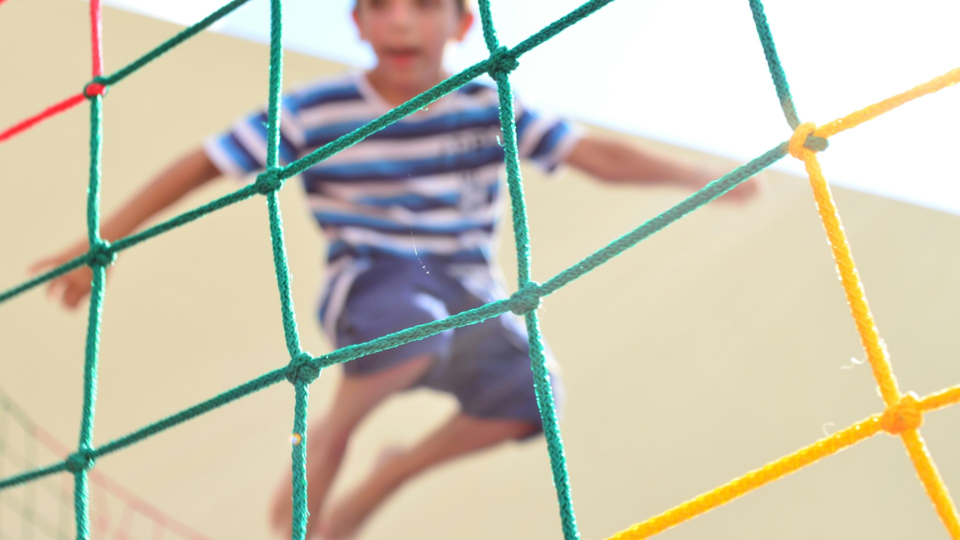 Child jumping on a trampoline behind a safety net.