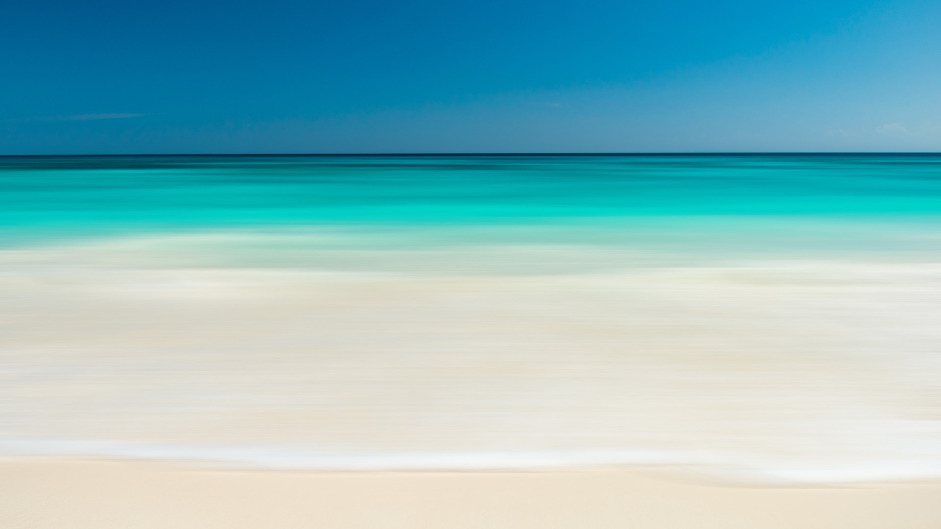 Calm turquoise ocean meeting a sandy beach under a clear blue sky.