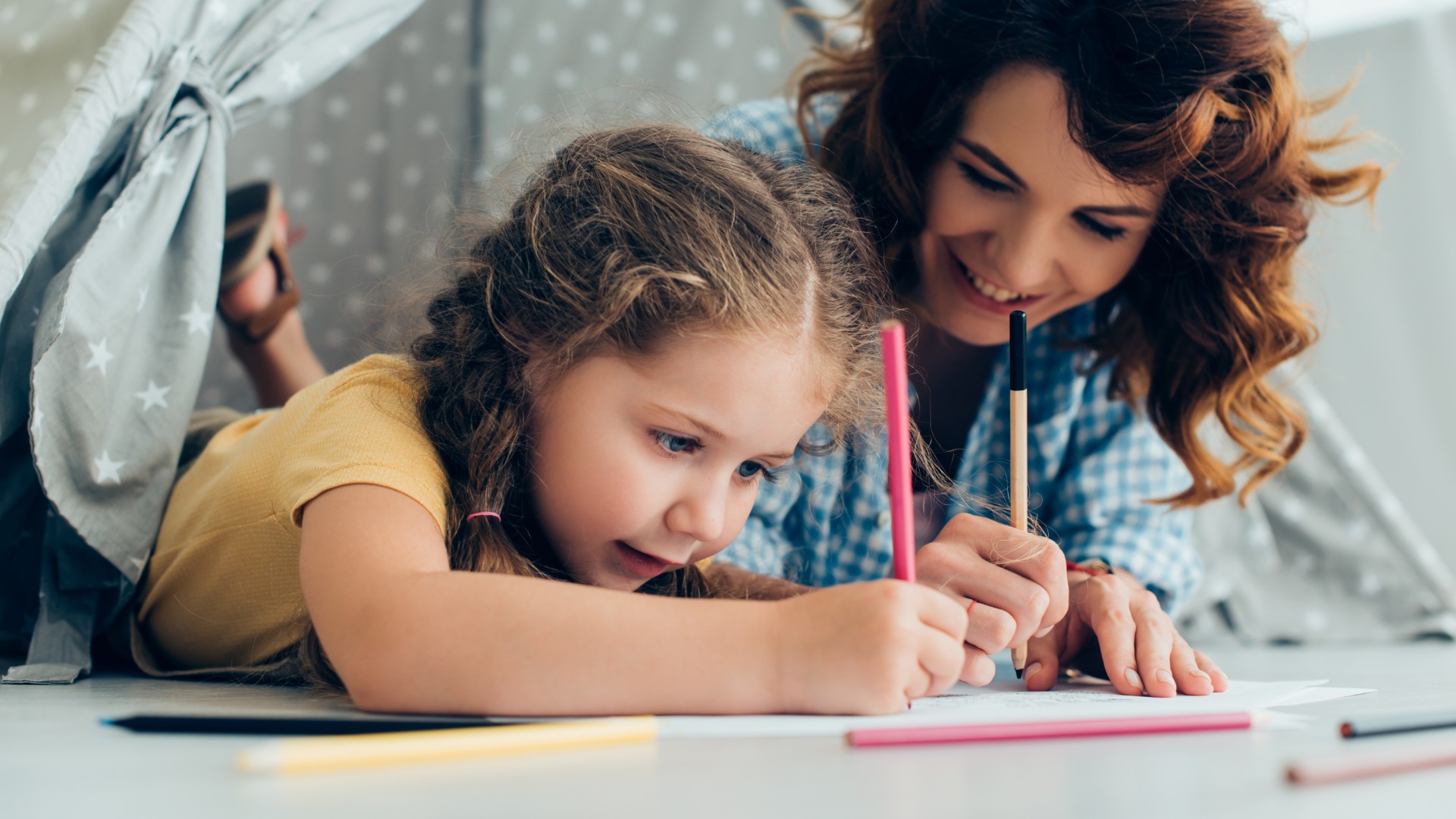 Adult and child drawing together with colored pencils on paper.
