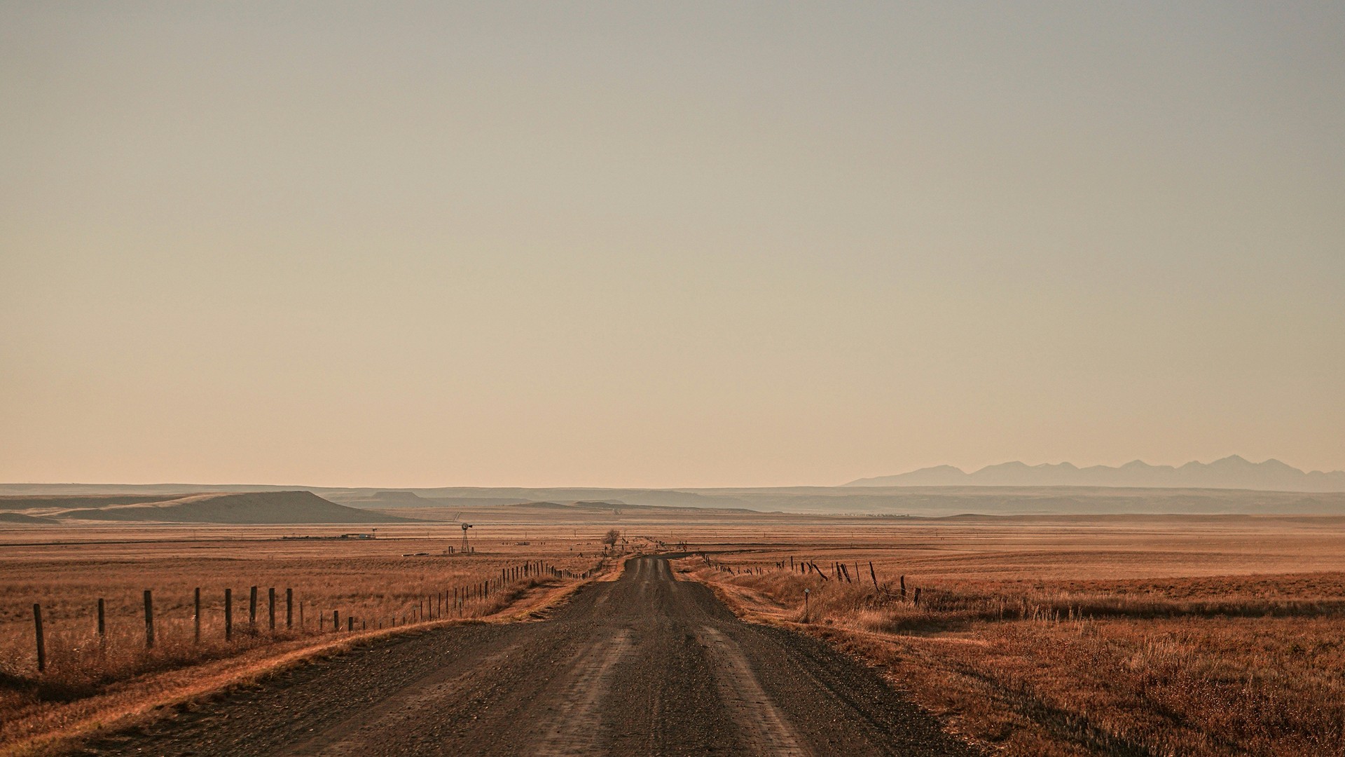 Long rural road stretching through open plains with distant mountains on the horizon.