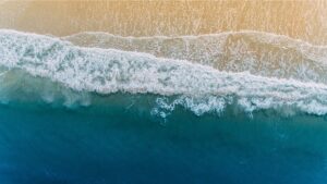 Aerial view of ocean waves rolling onto a sandy beach with turquoise water and white sea foam.