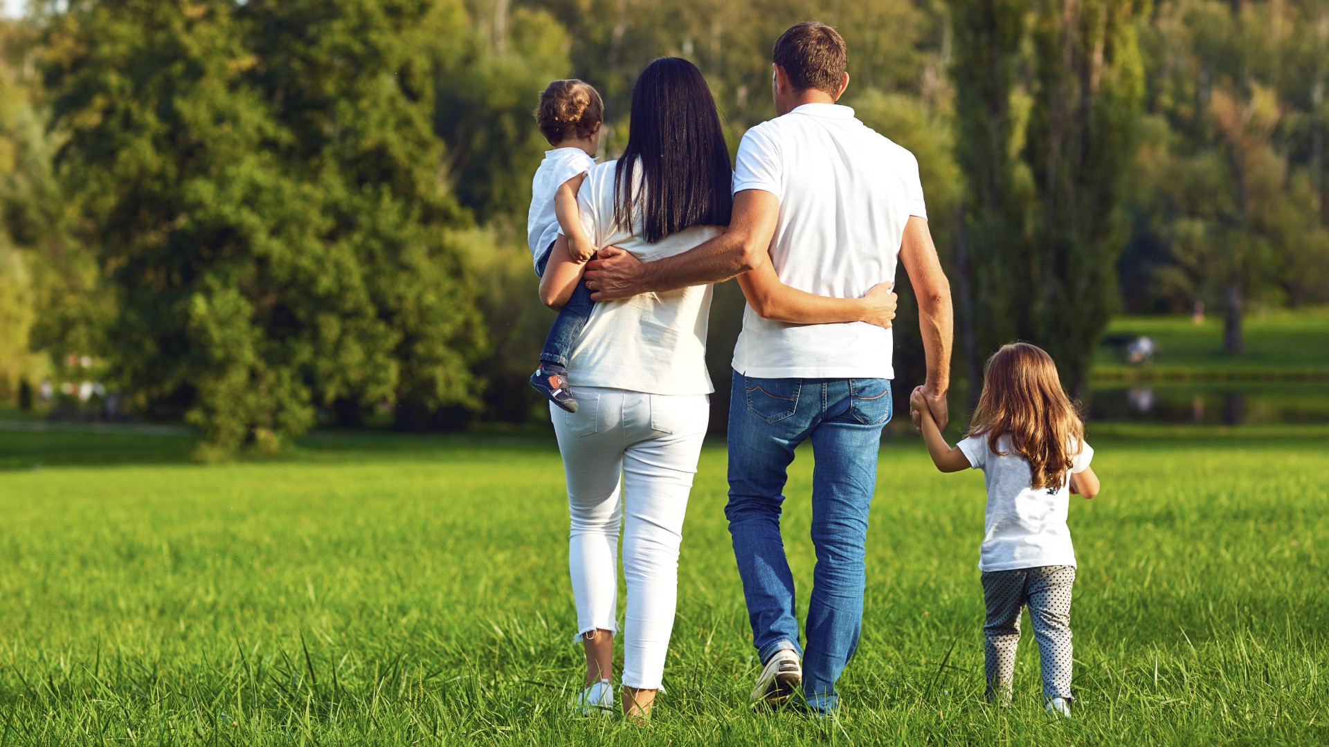 Family of four walking together in a green park, parents holding their children as they walk away
