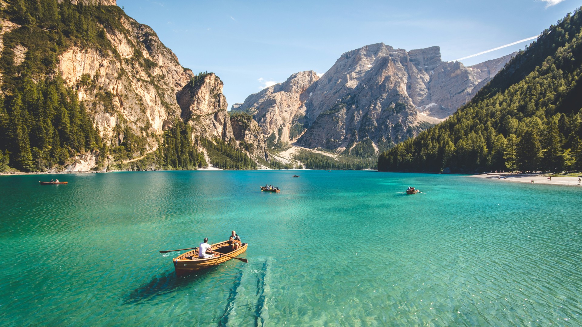 Wooden rowboats on a crystal-clear turquoise mountain lake surrounded by towering rocky peaks and evergreen forests.