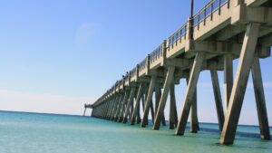 Long concrete fishing pier extending over calm turquoise ocean water beneath a clear blue sky.