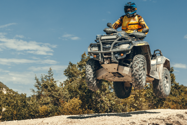 Rider in full gear jumping an ATV off a dirt trail in Montana backcountry on a sunny day