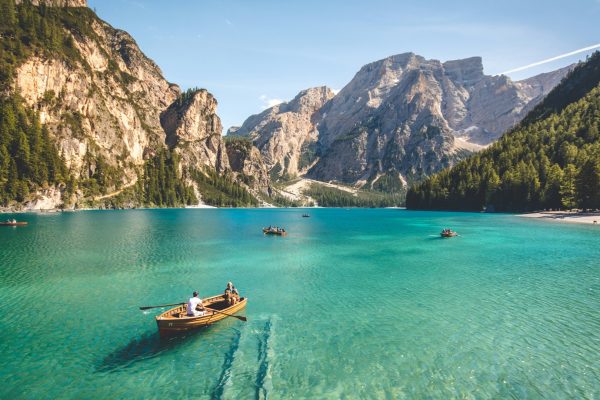 Wooden rowboats on a crystal-clear turquoise mountain lake surrounded by towering rocky peaks and evergreen forests.
