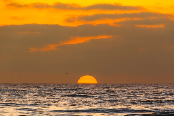 Un sol anaranjado que se hunde en el horizonte del océano bajo un cielo dorado y nublado