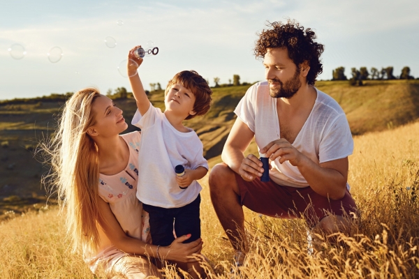 Una madre, un padre y su hijo pequeño haciendo pompas juntos en un prado dorado al atardecer
