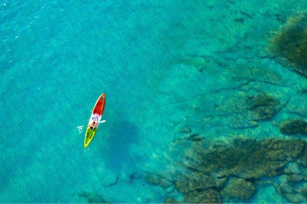 Aerial view of a colorful kayak floating over clear turquoise water near a rocky shoreline.