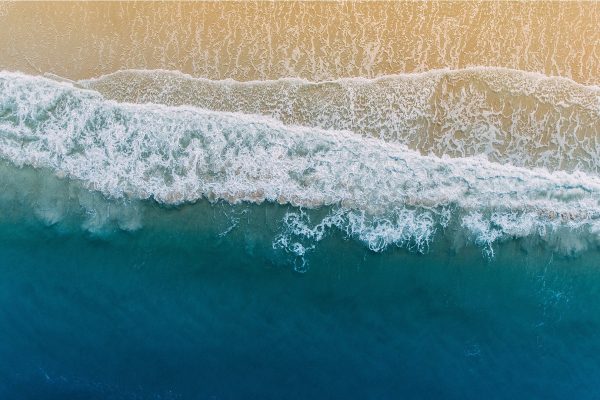 Aerial view of ocean waves rolling onto a sandy beach with turquoise water and white sea foam.