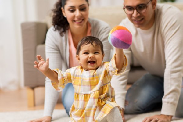 Smiling baby playing with a colorful ball while parents watch nearby in a living room.