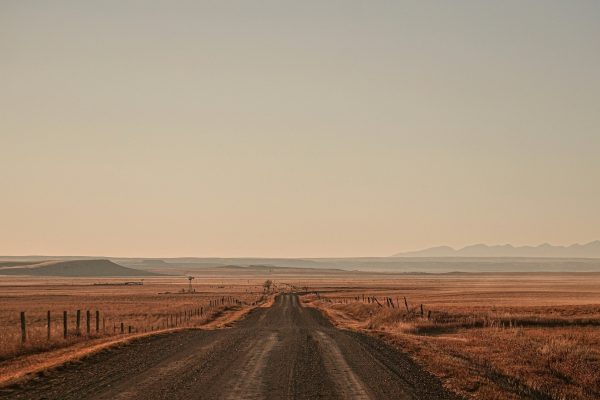 Long rural road stretching through open plains with distant mountains on the horizon.