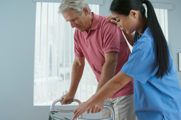 A healthcare worker assisting an elderly man with a walker during rehabilitation in a medical setting.