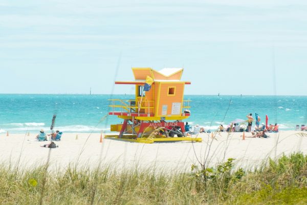 Colorful lifeguard tower on a sunny beach with beachgoers relaxing beside turquoise ocean waters.