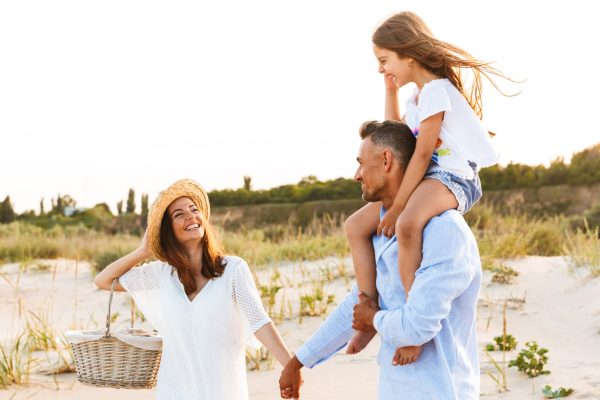 Happy family walking together on sandy dunes with a child riding on her father’s shoulders.