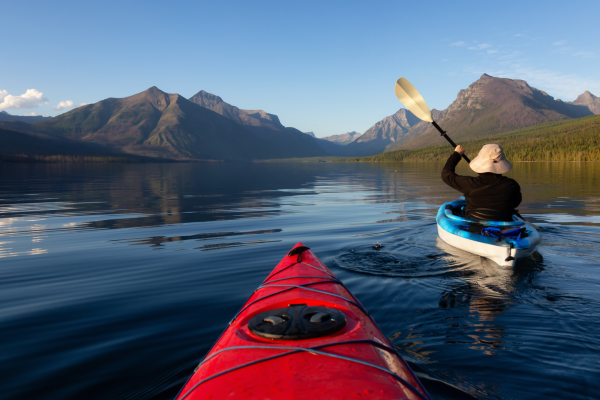 Two kayakers paddling on a calm Montana lake surrounded by mountains during summer