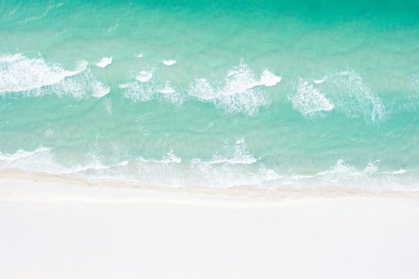 Aerial view of gentle turquoise ocean waves washing onto a wide white sand beach.