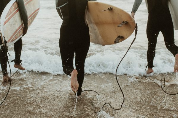 Surfers in wetsuits carrying surfboards as they run into the ocean through breaking waves.