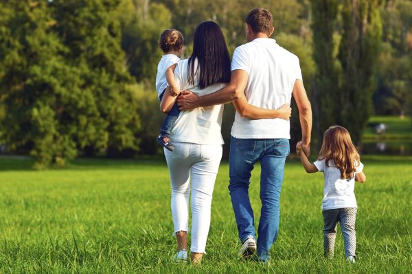 Family of four walking together in a green park, parents holding their children as they walk away