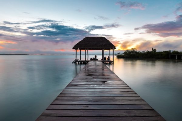 Un embarcadero de madera que conduce a un pabellón con techo de paja sobre aguas tranquilas al atardecer