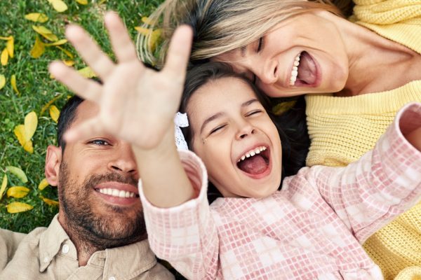 Una feliz familia de tres miembros riendo juntos mientras están tumbados en la hierba